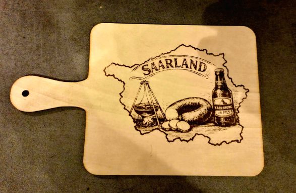 Holzbrett mit der Umrisskarte von Saarland und regionalen Spezialitäten.